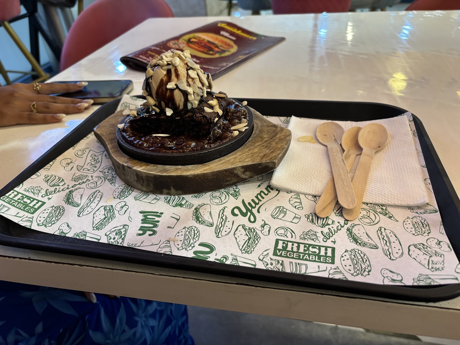 A brownie sizzler on a cast-iron plate and wooden base, served on a tray with wooden spoons
