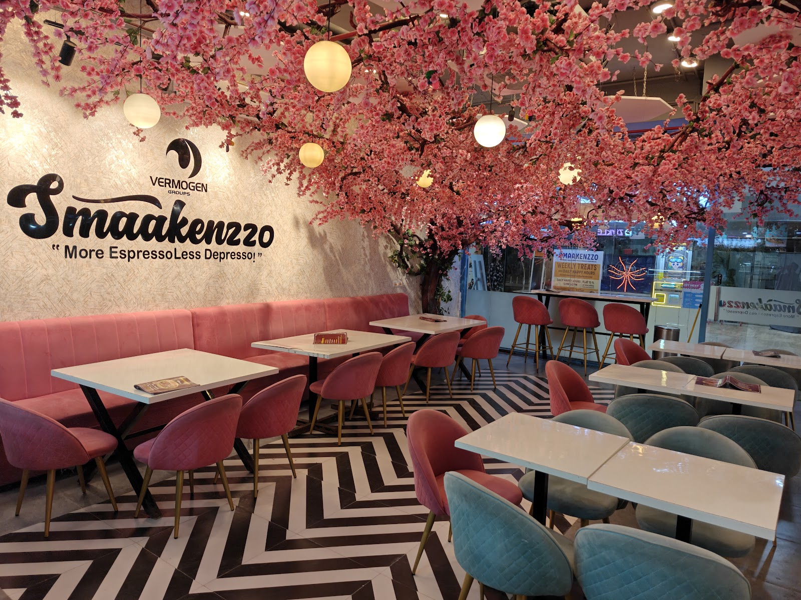The Gachibowli room under a full cherry-blossom canopy: dusty pink and sage velvet chairs, marble-topped tables, a black-and-white chevron floor and warm globe pendants
