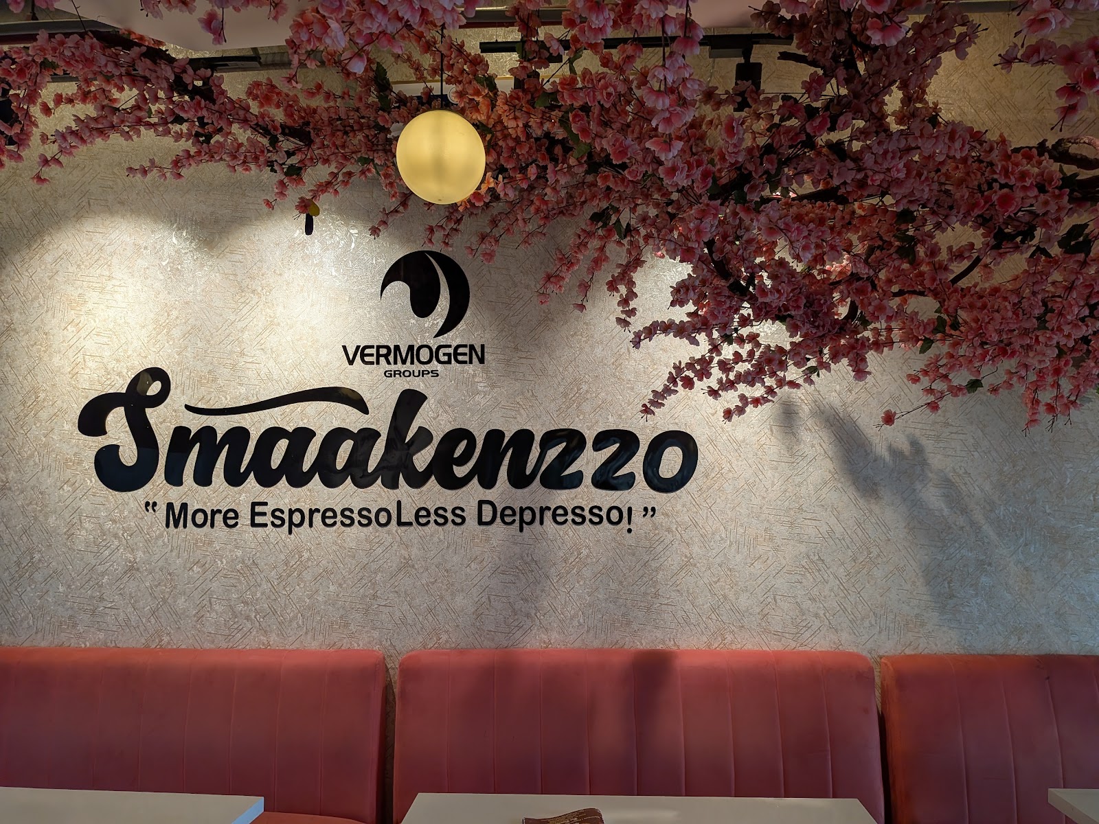 The feature wall: the Smaakenzzo wordmark in black, above the line "More Espresso Less Depresso!", with blossom branches overhead