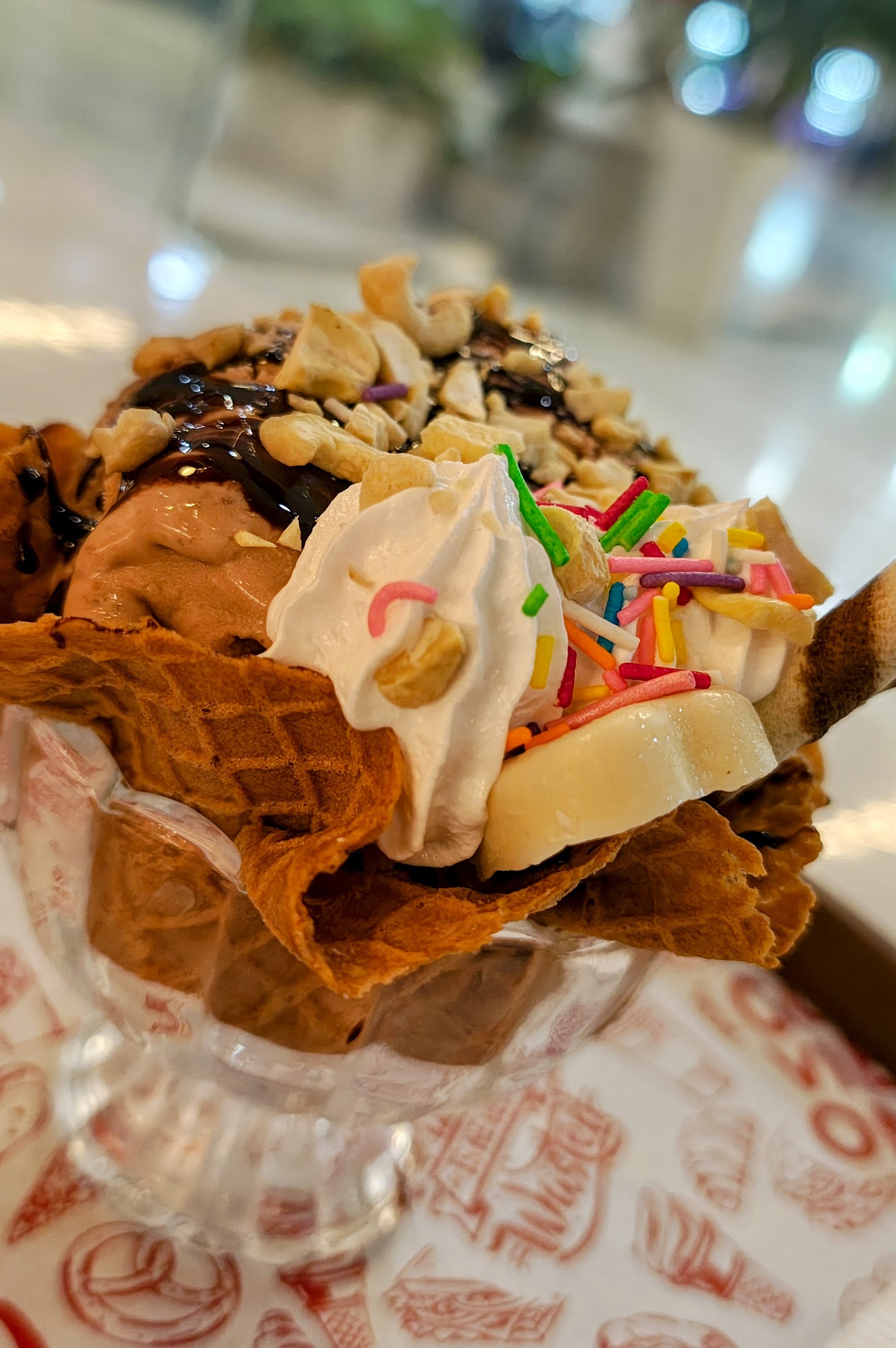 A sundae in a waffle bowl, loaded with cashews, chocolate sauce and sprinkles
